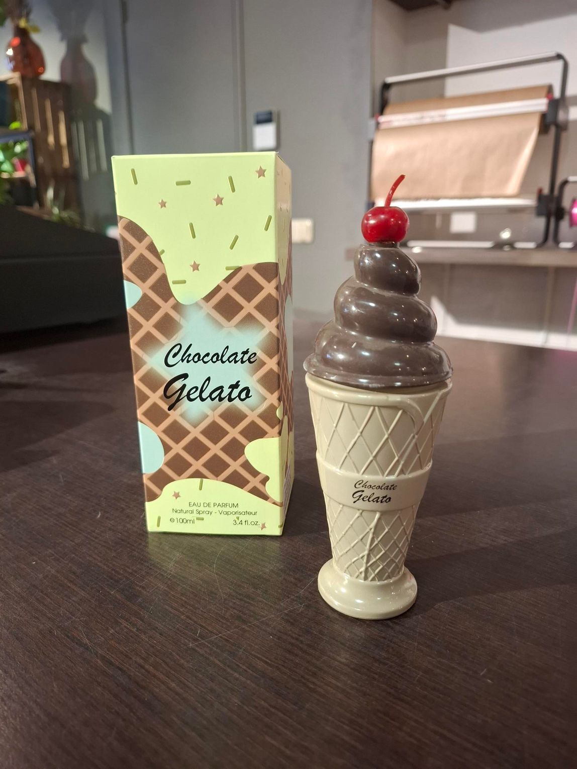 Een presentatie van pastelkleurige, ijsvormige kaarsen in wafelvormpjes op een zwarte plank, met daarachter kleurrijke verpakkingen.