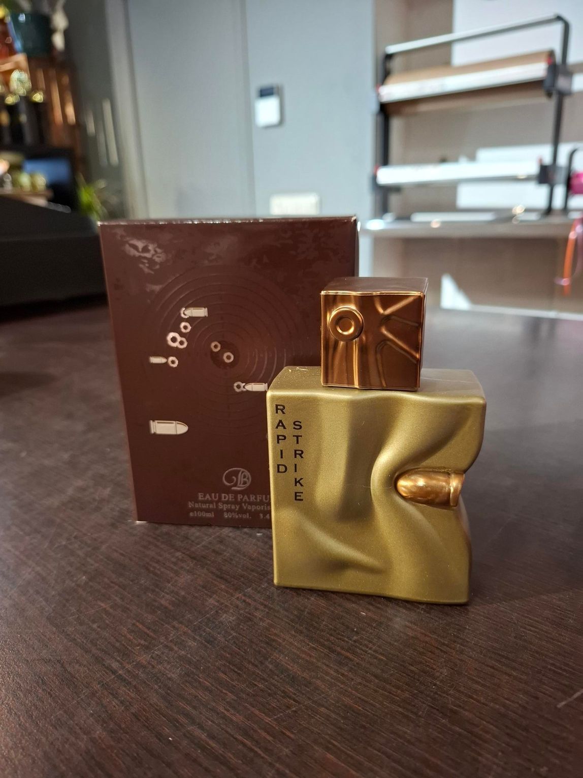 Gouden parfumflesje met bruine doos op een tafel in een lichte kamer.