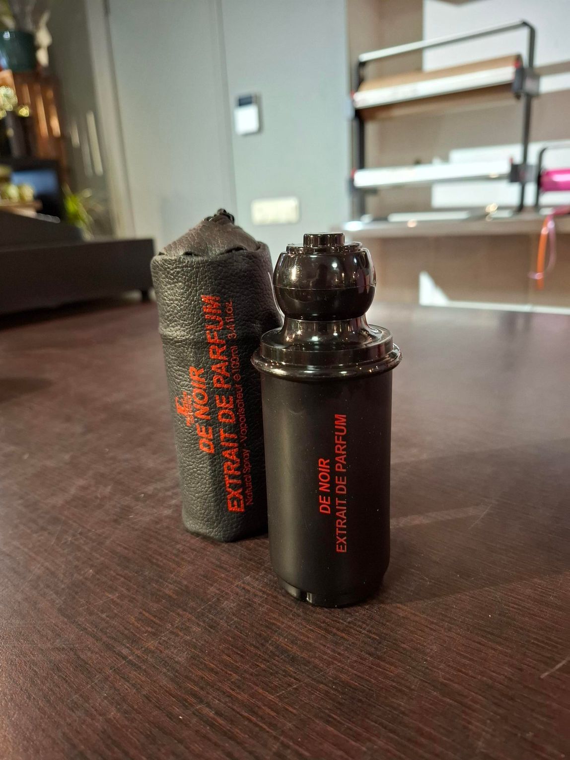Twee zwarte cilindrische flessen met rode tekst op een houten tafel binnen.