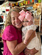 a woman is holding a baby girl with a pink bow on her head .