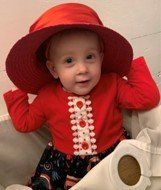 a baby wearing a red hat and a red shirt is sitting next to a roll of toilet paper .