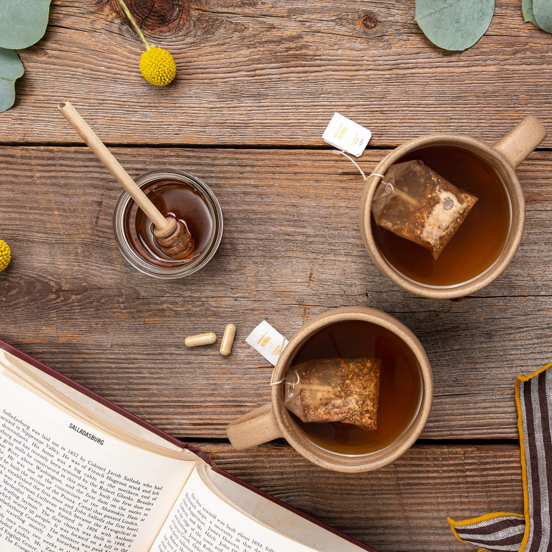 two cups of tea are on a wooden table next to a book