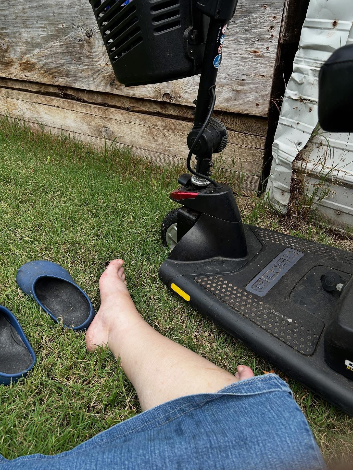 A person is laying on the grass next to a mobility scooter.