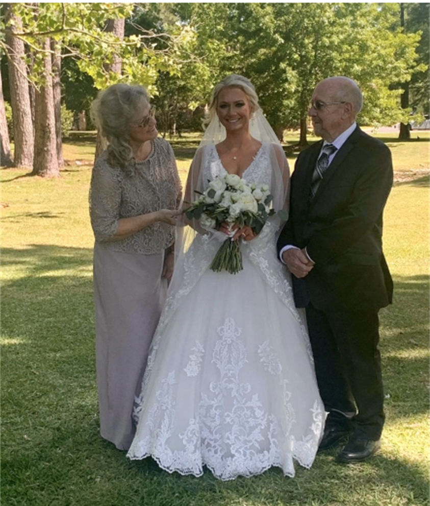 a bride and her parents are posing for a picture in a park .