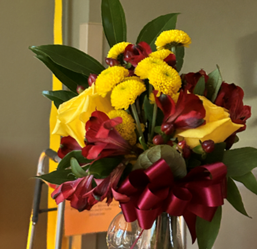 A vase filled with yellow and red flowers with a red bow