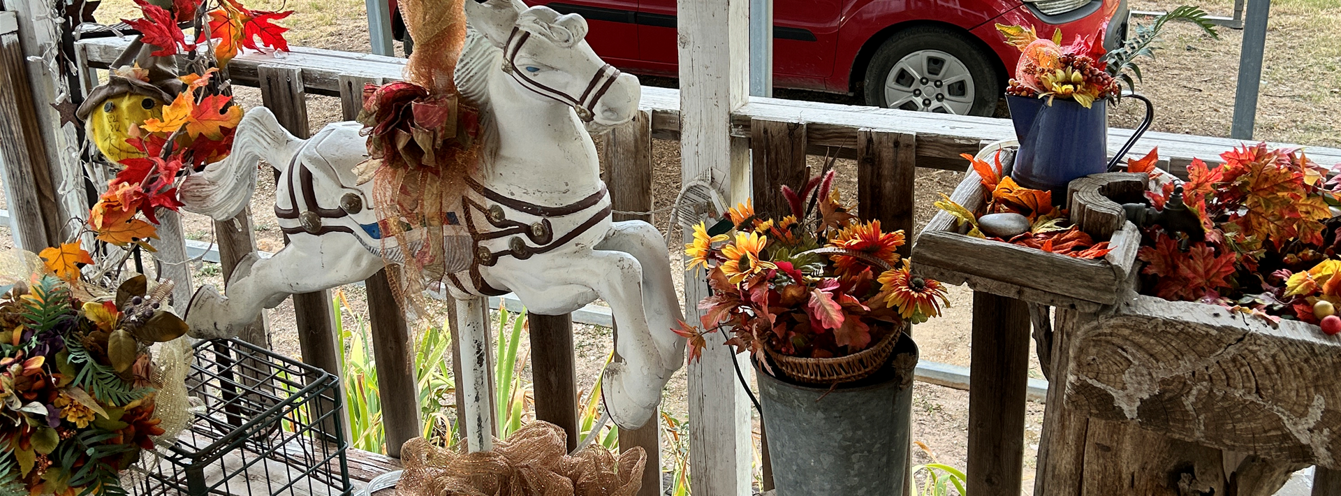 A white rocking horse is sitting on a porch surrounded by flowers.