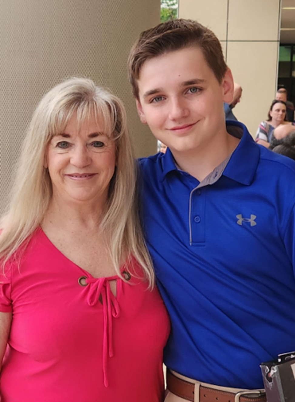 a boy in a blue under armour shirt stands next to a woman in a pink shirt