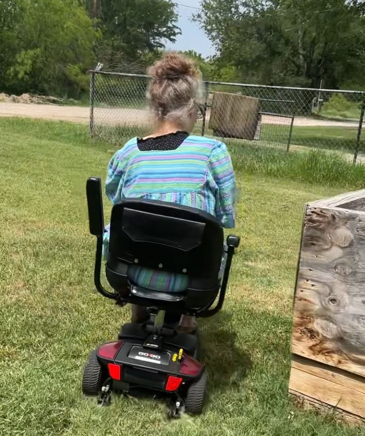 A woman is sitting on a mobility scooter in the grass.