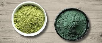 Two bowls of green powder are on a wooden table.