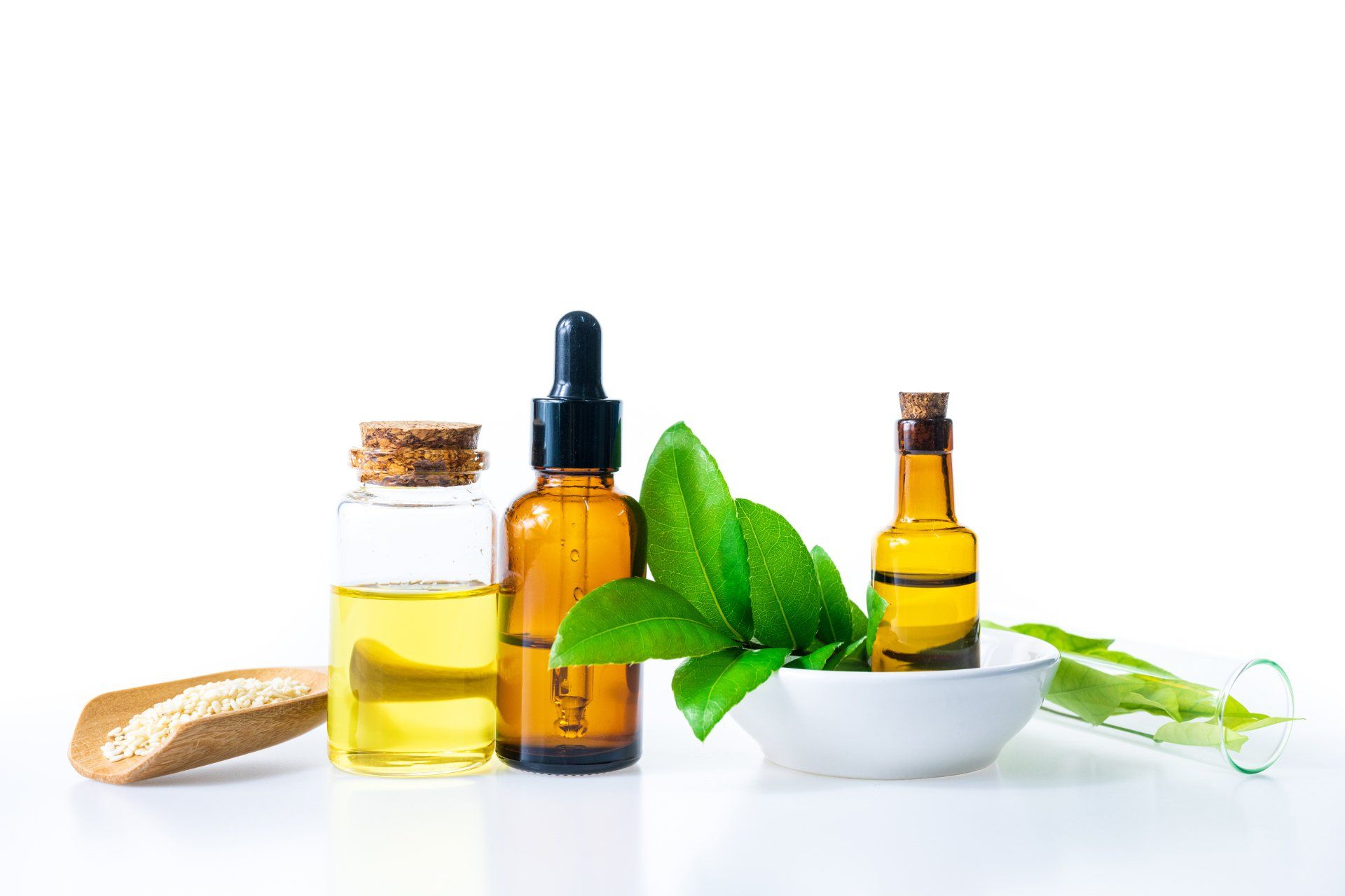 three bottles of essential oil with leaves in a bowl on a white background .
