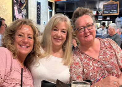 three women are posing for a picture while sitting at a table in a restaurant .