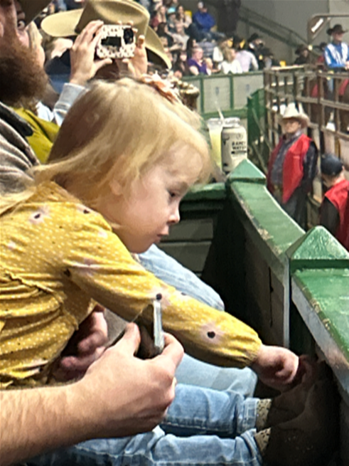 a little girl is sitting on a man 's lap at a rodeo