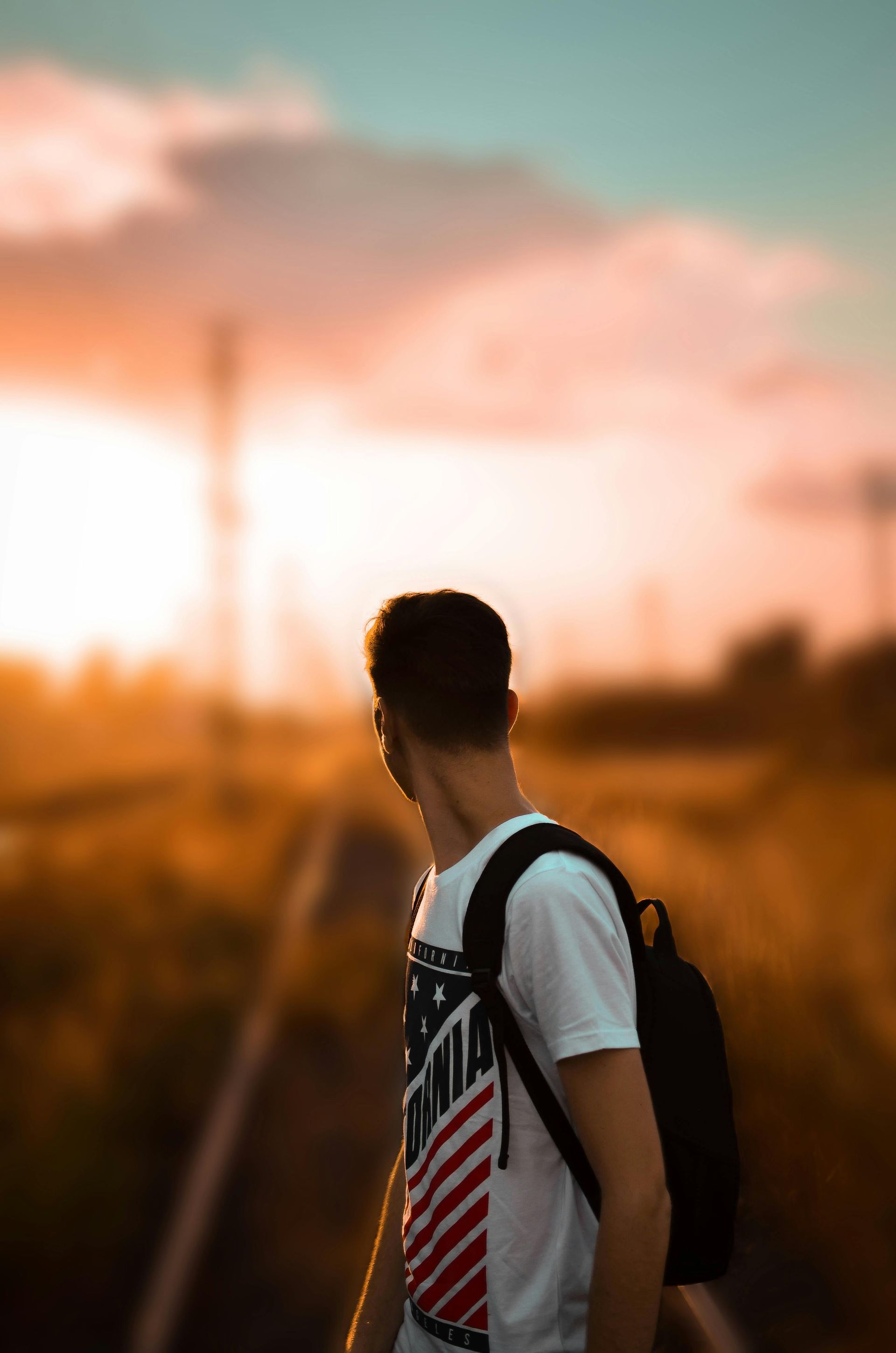 Person with backpack standing on train tracks, looking toward the sunset.