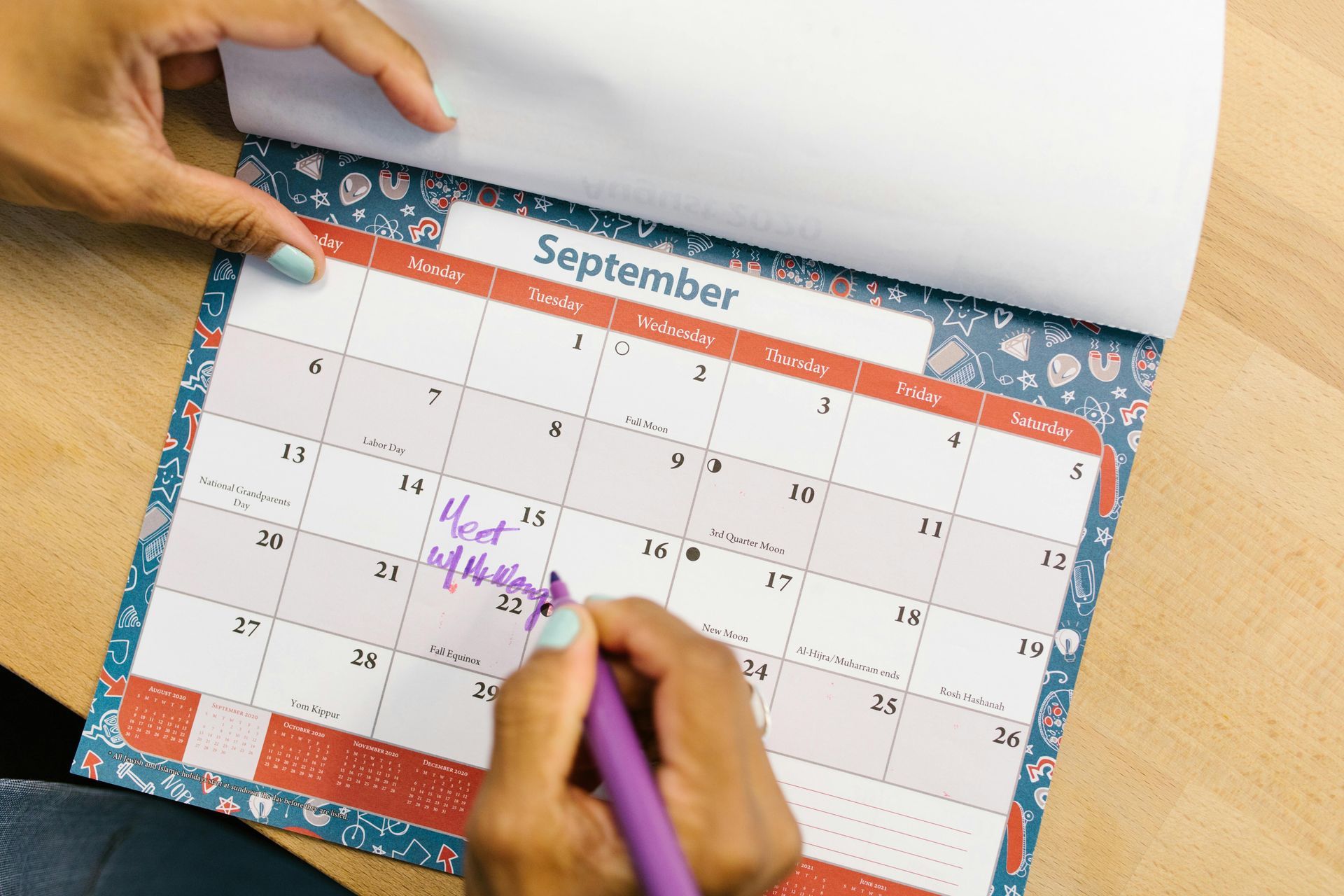 Person writing on a September calendar with a purple pen.