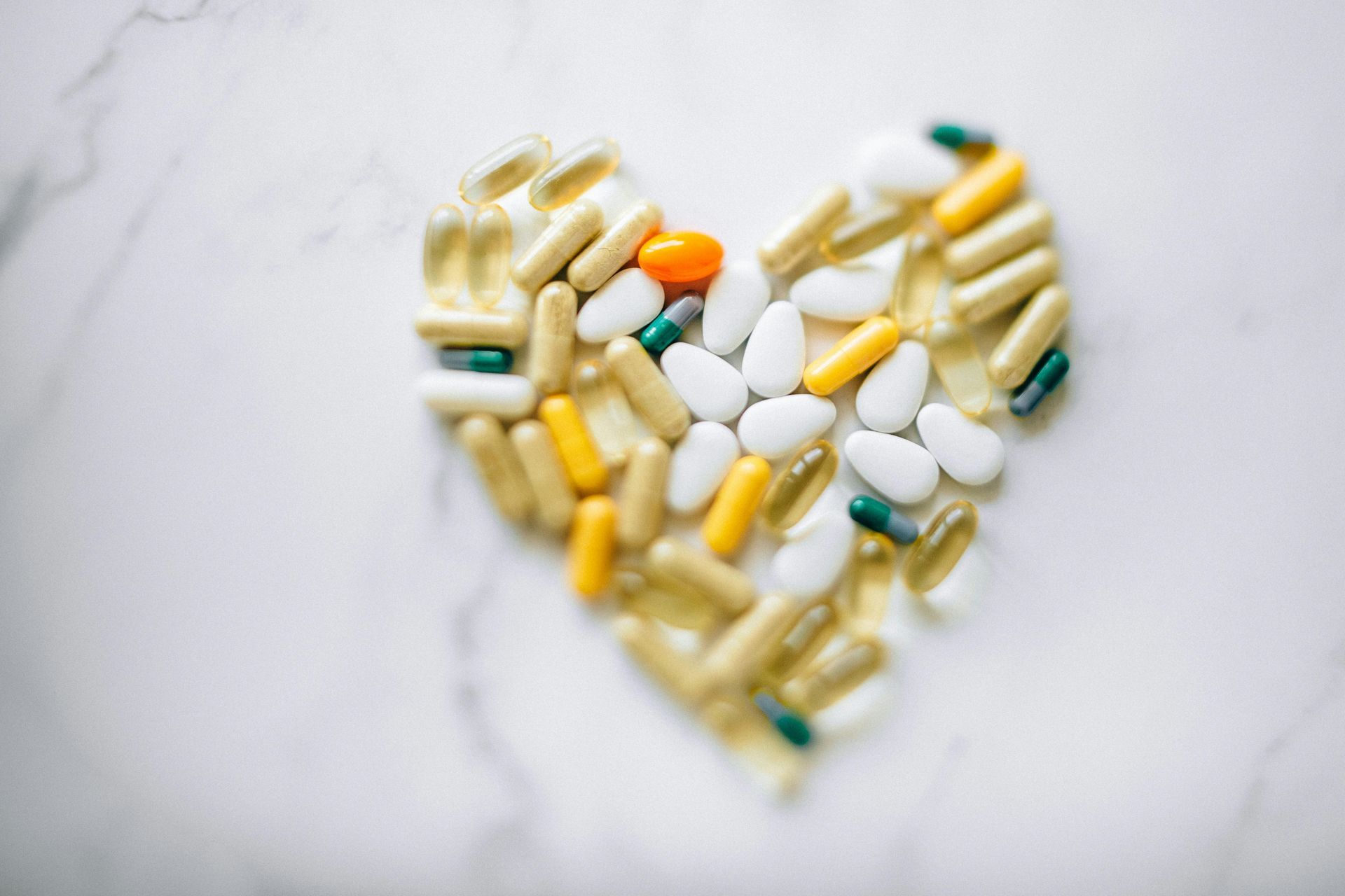 Pills of various colors and shapes arranged in a heart shape on a white marble surface.