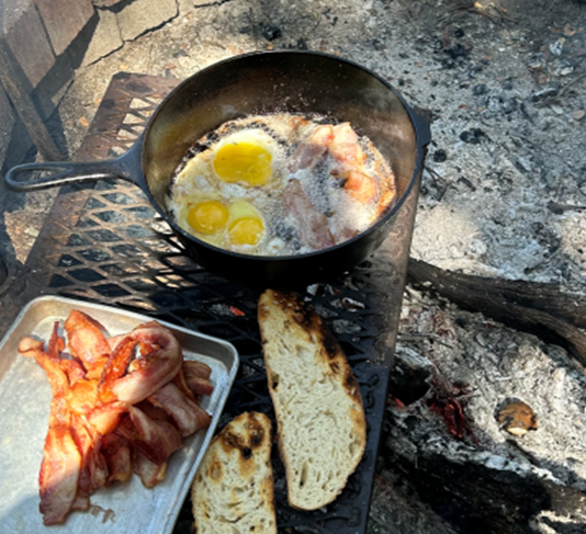 eggs and bacon are cooking in a skillet on a grill