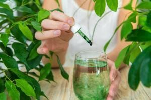 A woman is pouring a drop of green liquid into a glass of water.