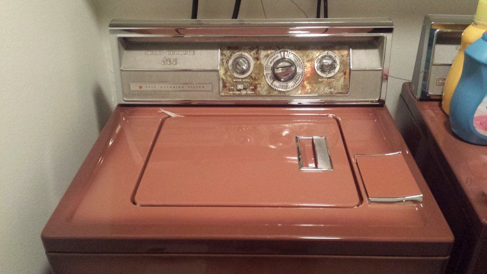 A red washing machine is sitting on a counter in a laundry room.