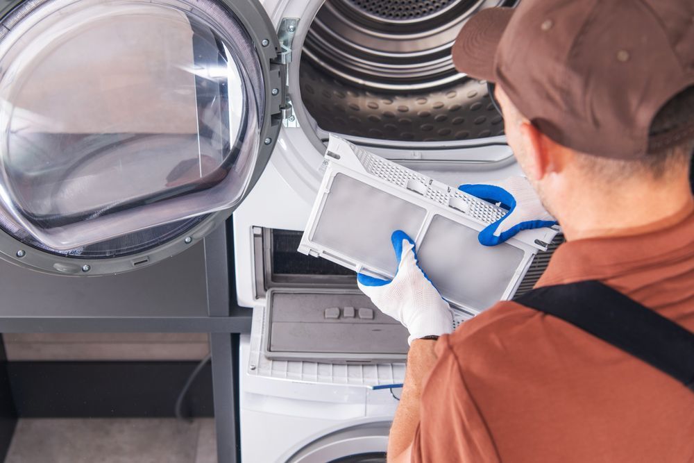 A man is holding a filter in front of a washing machine and dryer.
