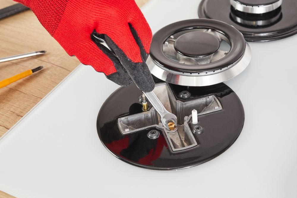A person is fixing a gas stove with a pair of pliers.