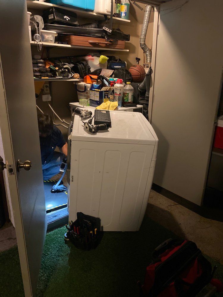 A person is working on a washer and dryer in a laundry room.