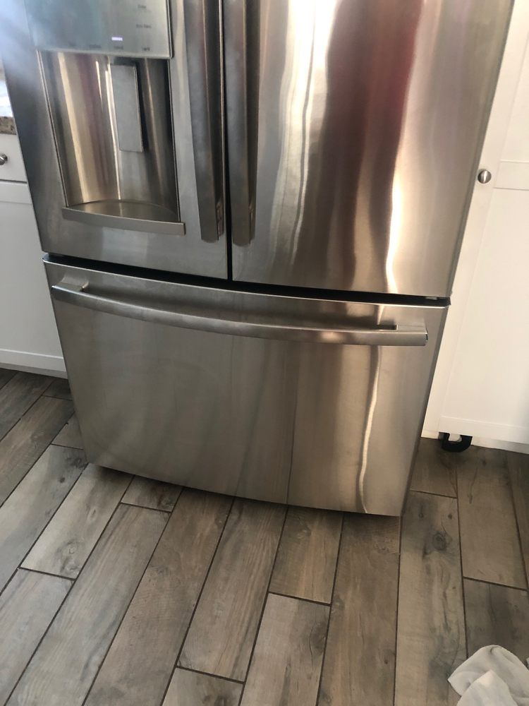 A stainless steel refrigerator is sitting on a wooden floor in a kitchen.
