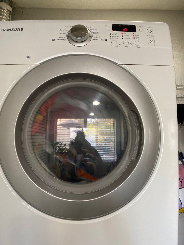A white washing machine is sitting in a laundry room next to a window.