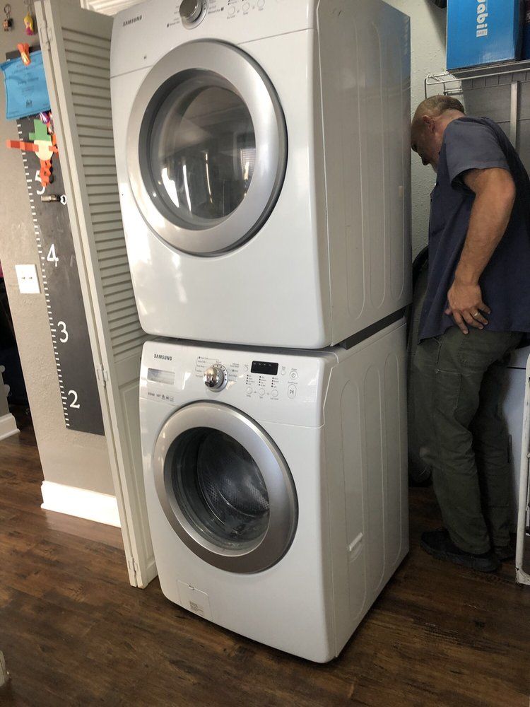 A man is standing next to a washer and dryer stacked on top of each other.