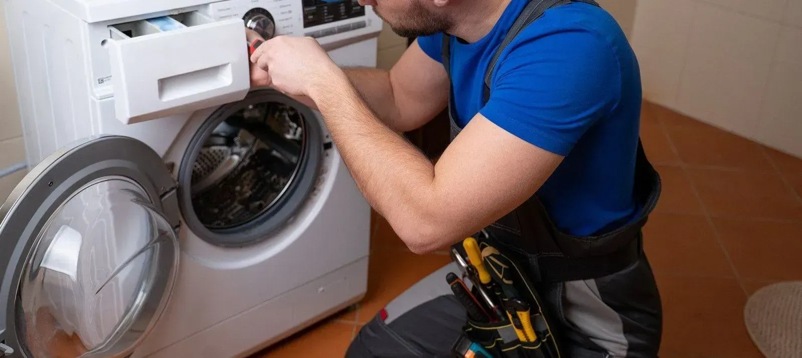 A man is fixing a washing machine in a bathroom.