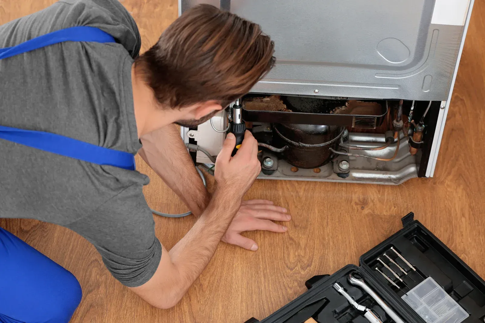 A man is working on a refrigerator on the floor.