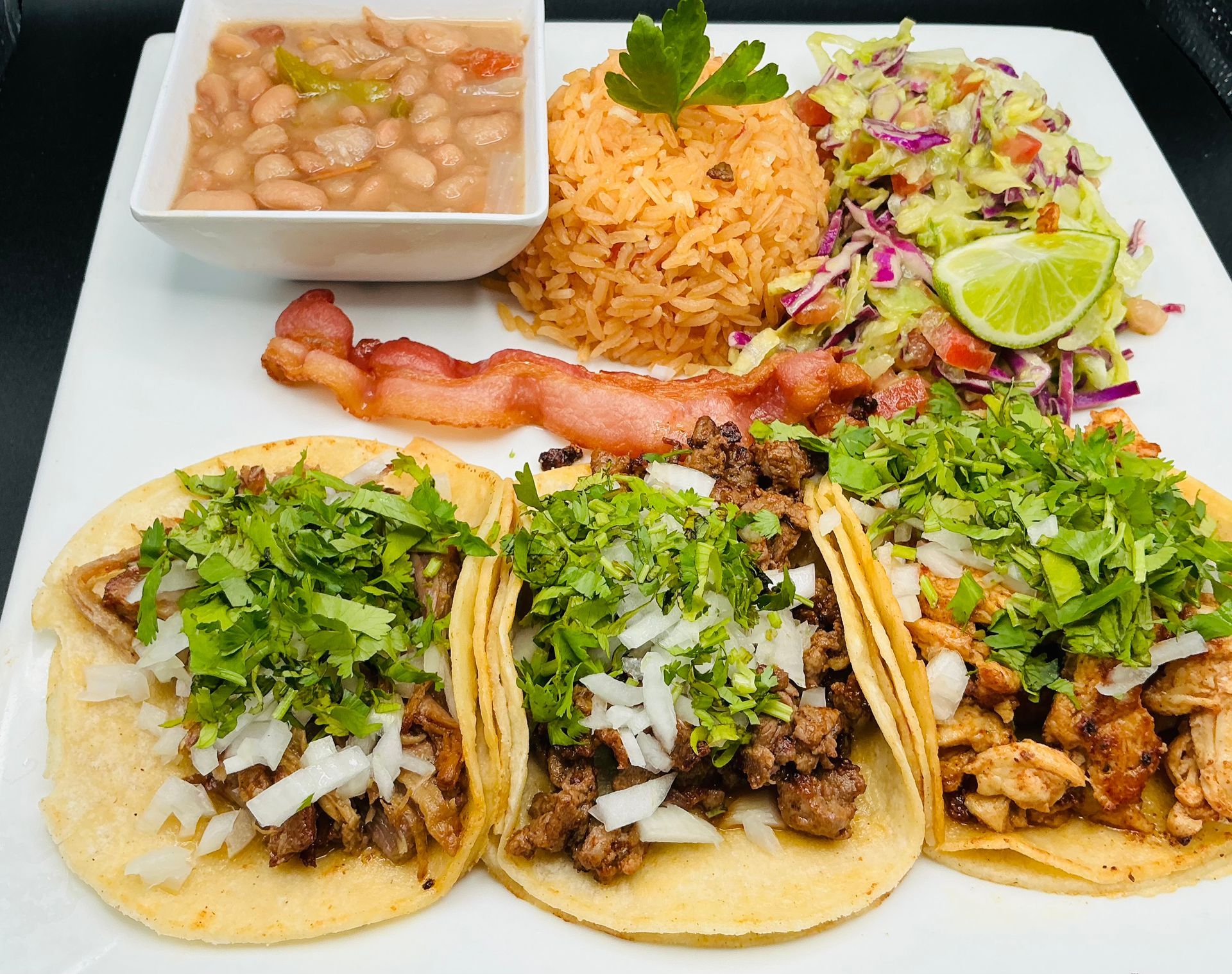 Plate of Mexican food: tacos, rice, beans, bacon, and slaw.