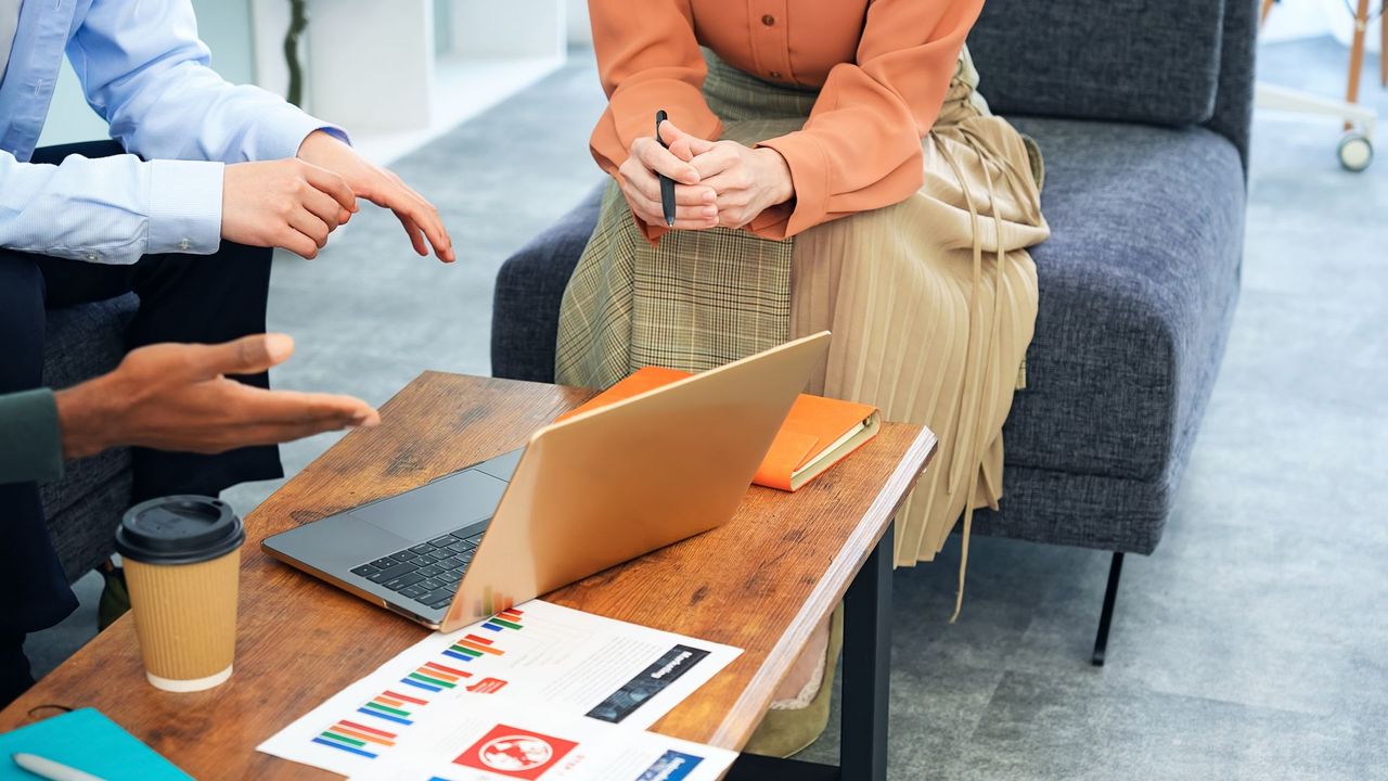 People discussing around a laptop on a coffee table with brochures and coffee in a meeting room