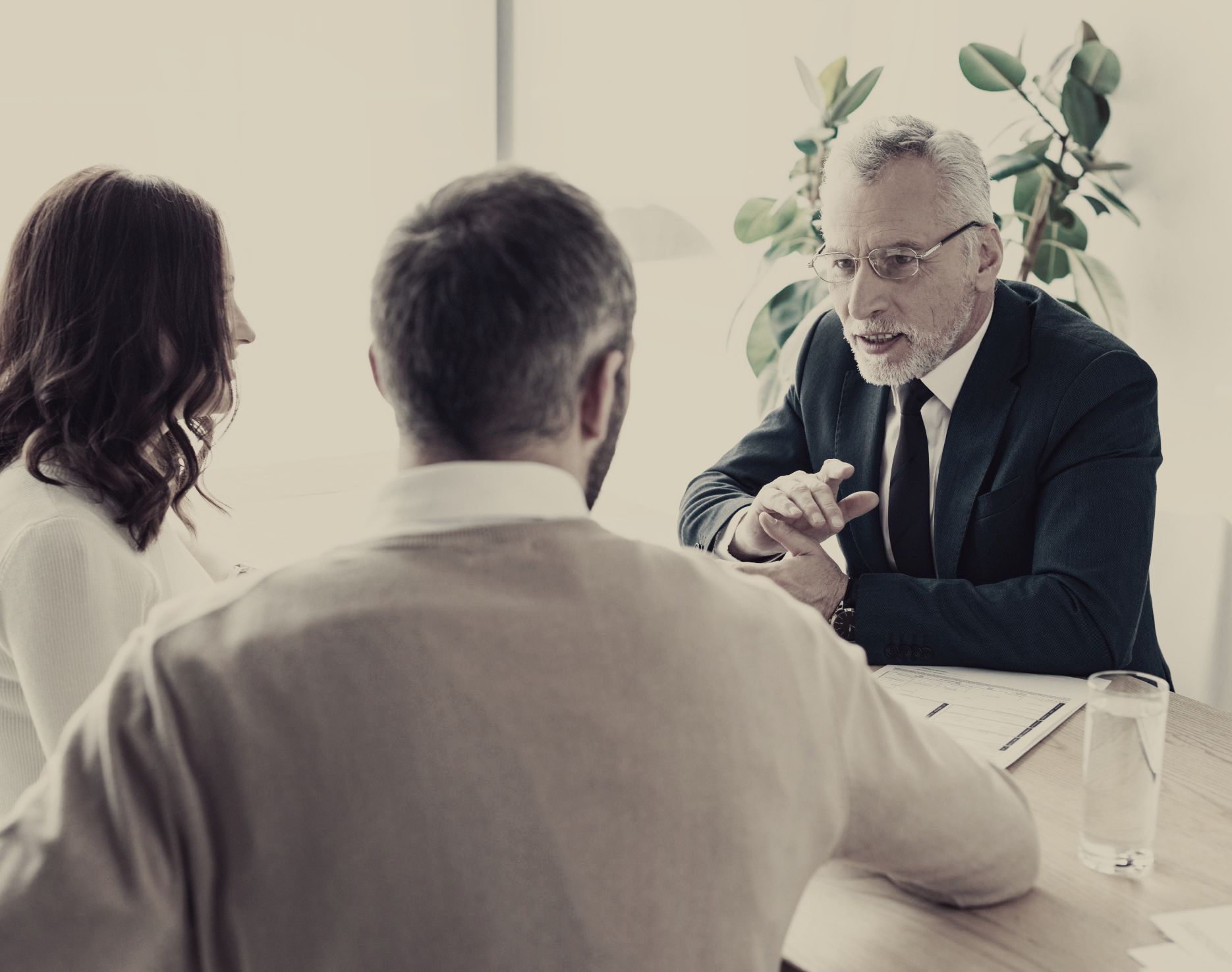 A man in a suit and tie is sitting at a table talking to a man and woman.