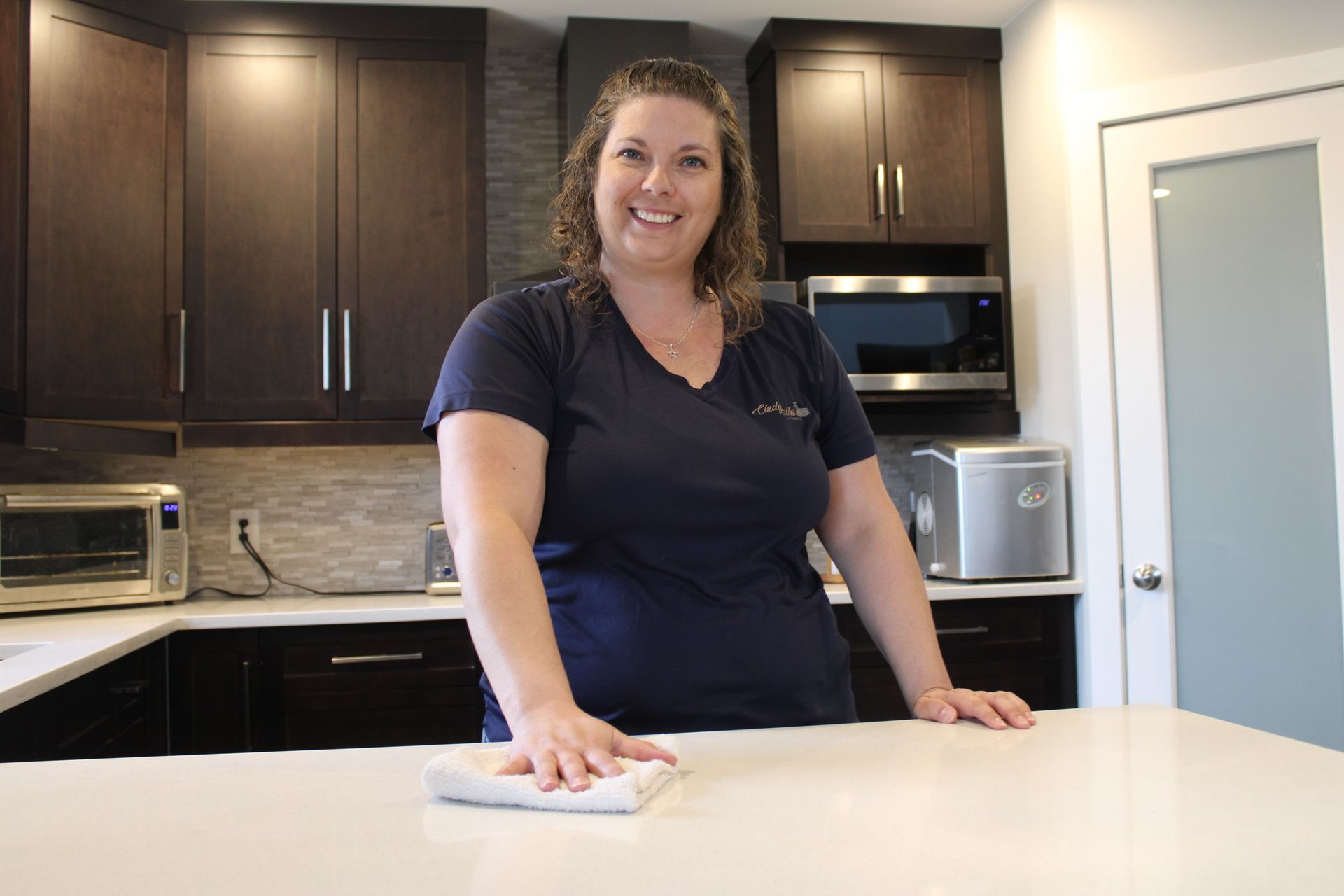 Woman cleaning a white kitchen countertop with a cloth, smiling in a modern kitchen.