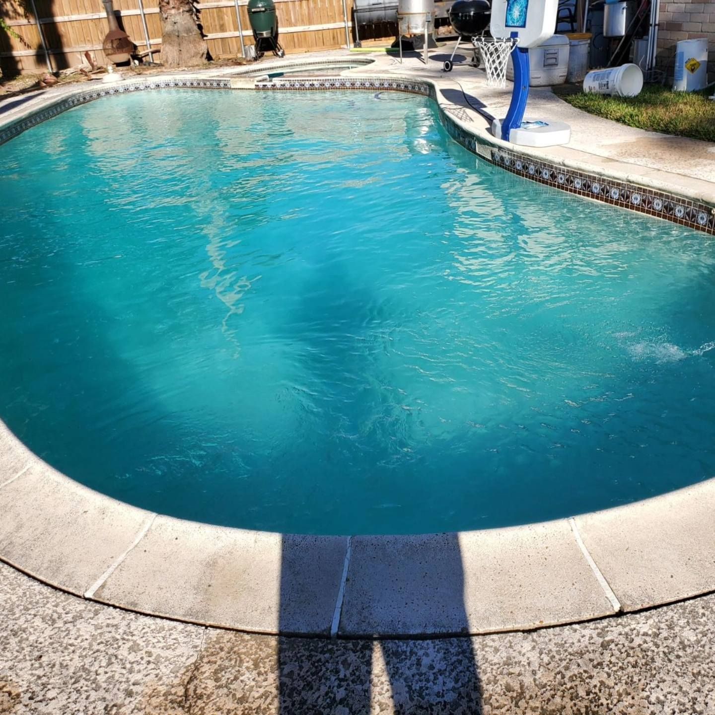 Backyard swimming pool with bright blue water and a shadow across the deck