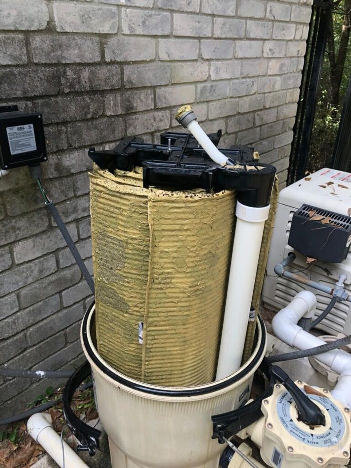 Outdoor HVAC unit with yellow insulation and white pipes beside a brick wall