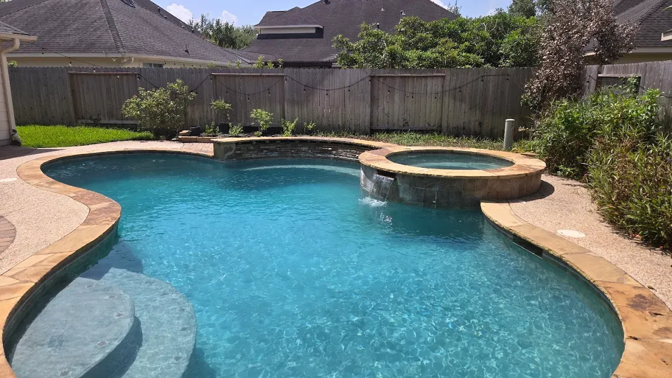 Backyard swimming pool with turquoise water, curved stone edges, and a raised circular spa under a sunny sky