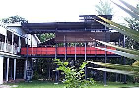 A large house with a red balcony is surrounded by trees and grass.