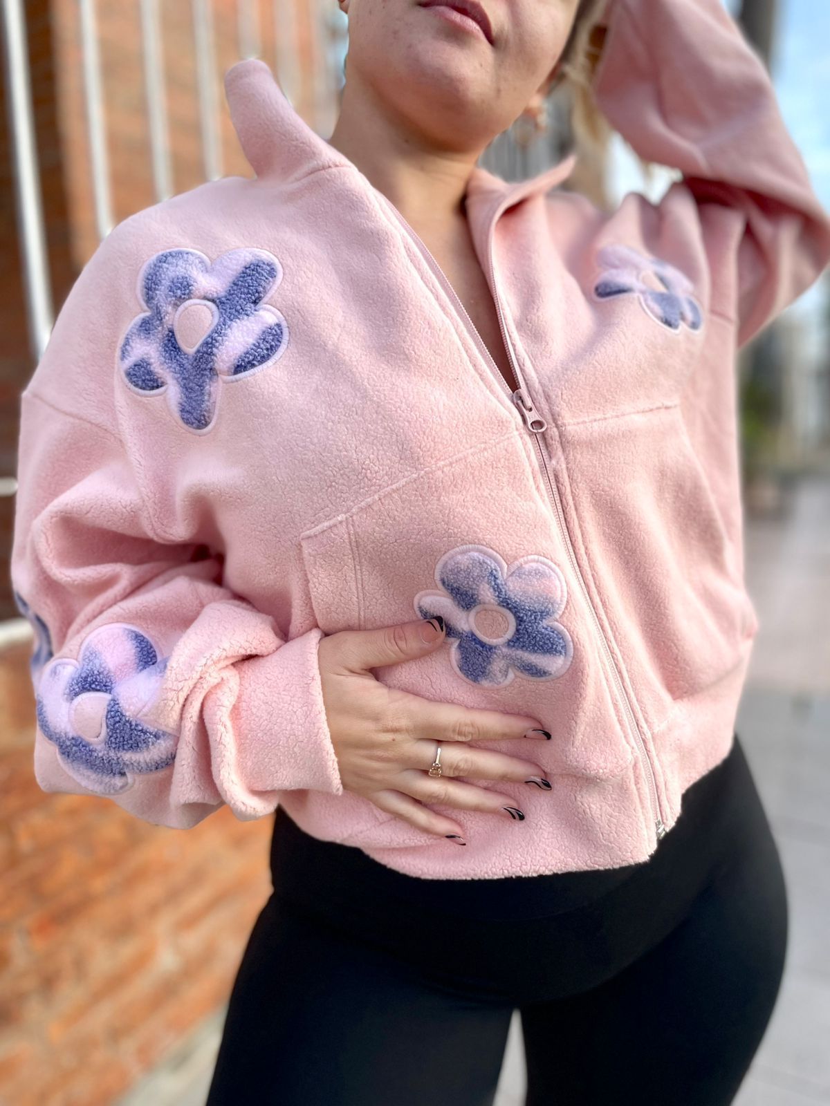 Una mujer lleva una chaqueta rosa con flores moradas en las mangas.