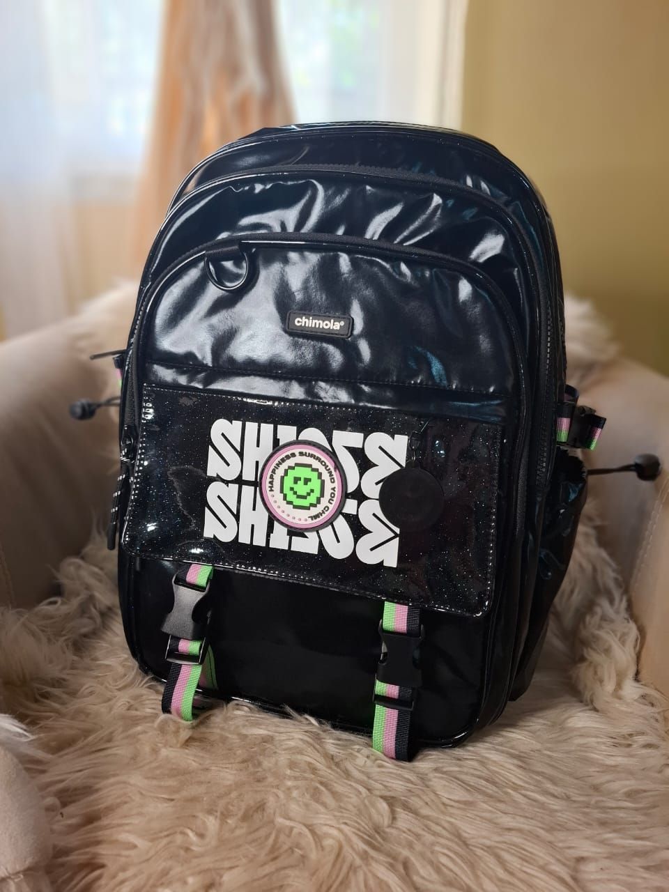 Una mochila negra con una cara sonriente está colocada sobre una silla.
