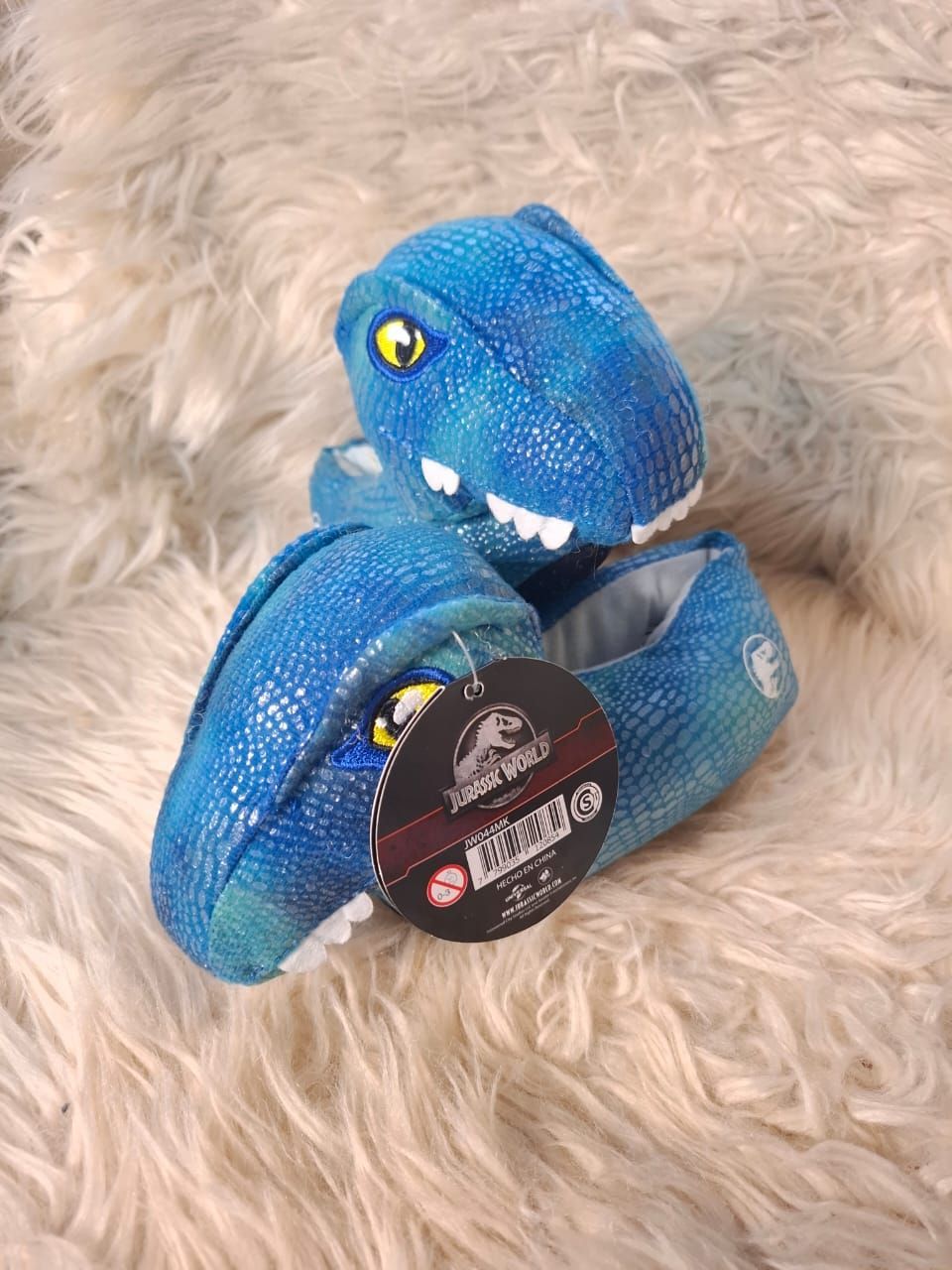 Un par de pantuflas de dinosaurio azules están sobre una superficie peluda.