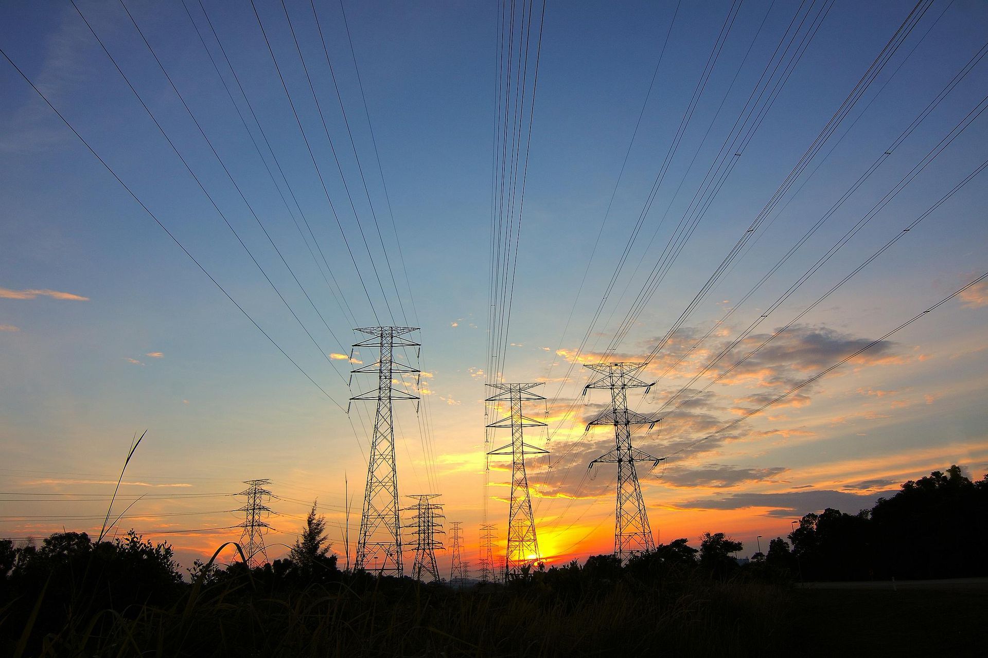 Sunset behind power lines and towers, with a flock of birds flying above.