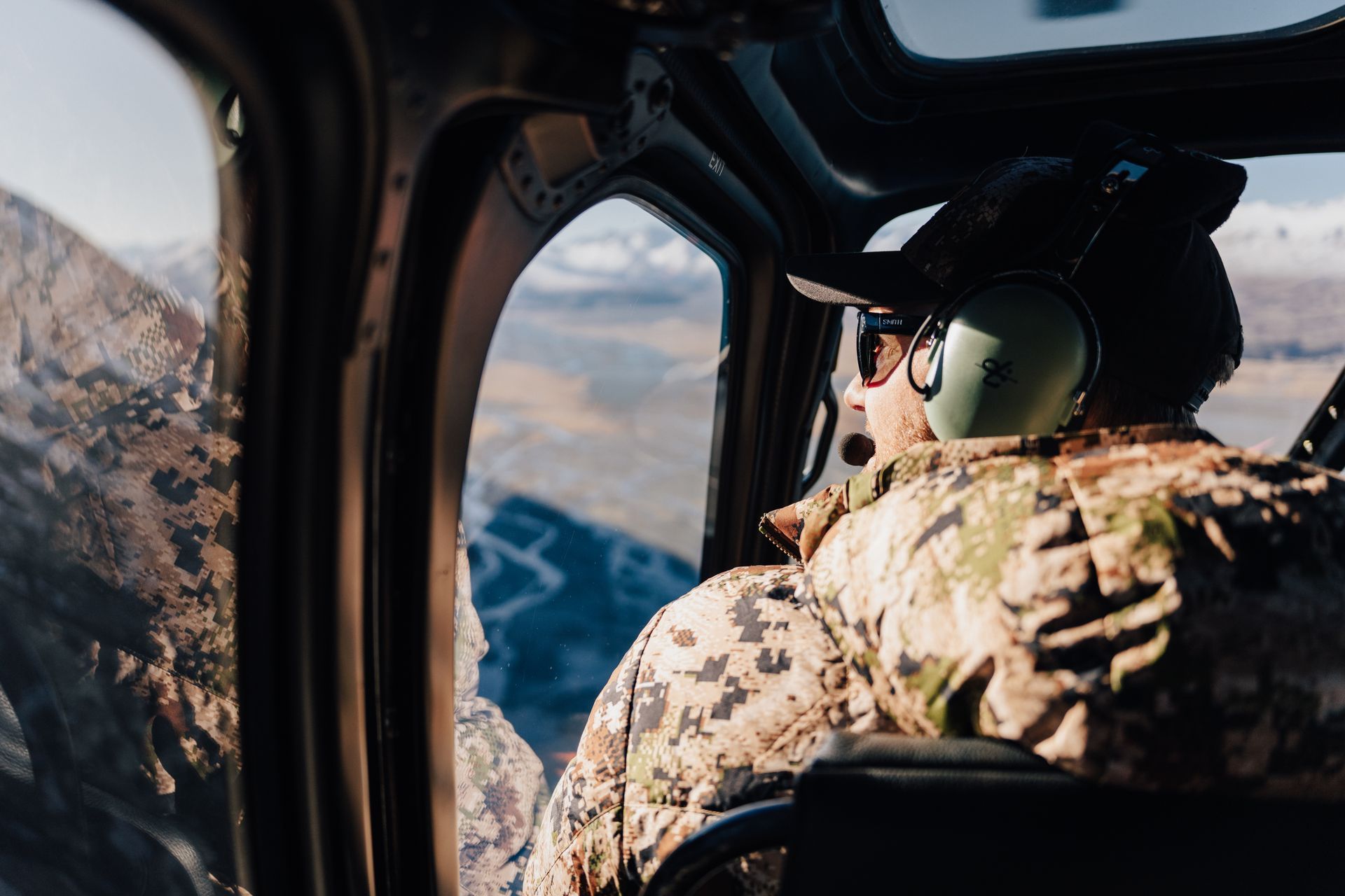 A man is sitting in the cockpit of a helicopter looking out the window. Rival Hunts NZ