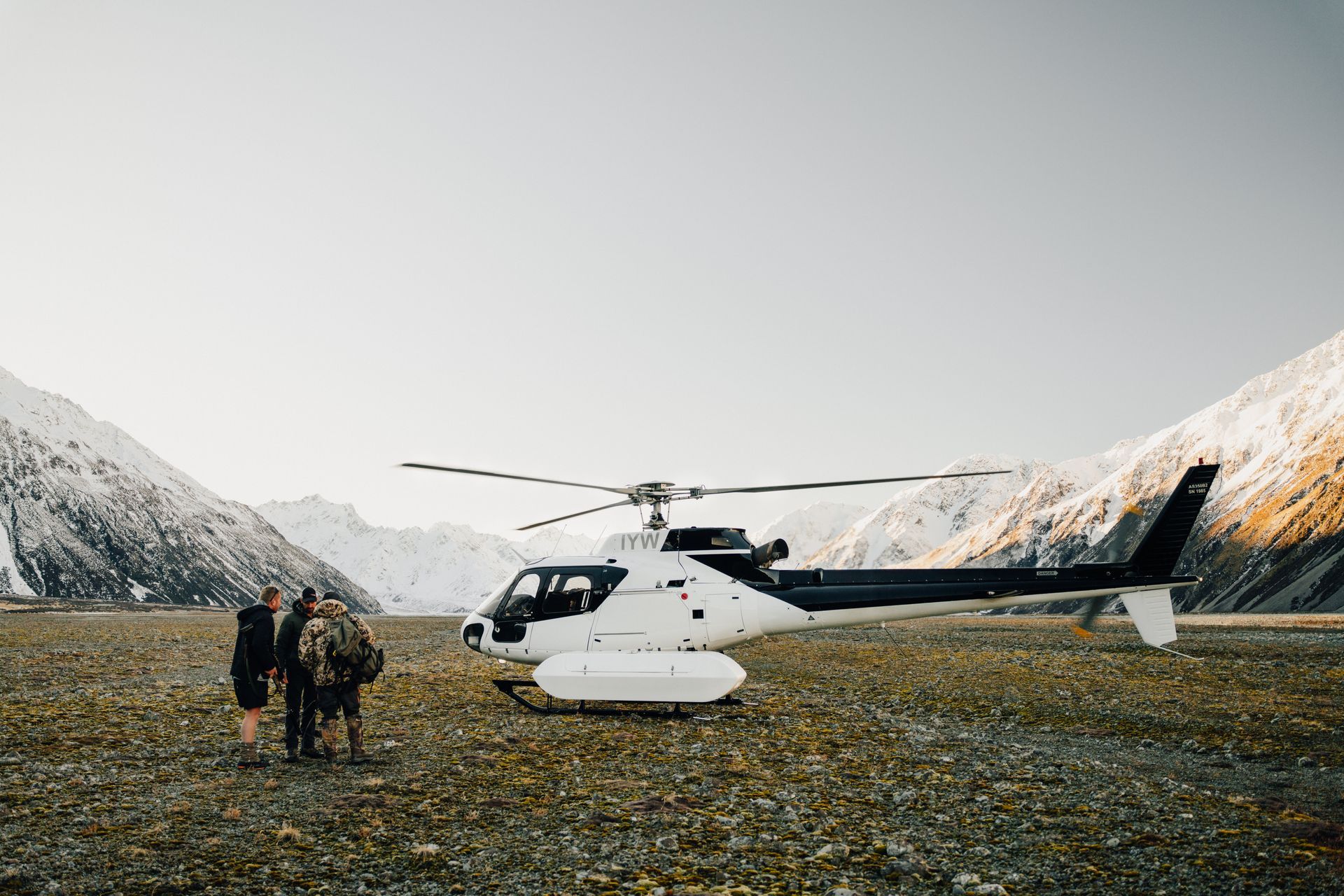 A group of people are standing next to a helicopter in a field. High Country Outfitters