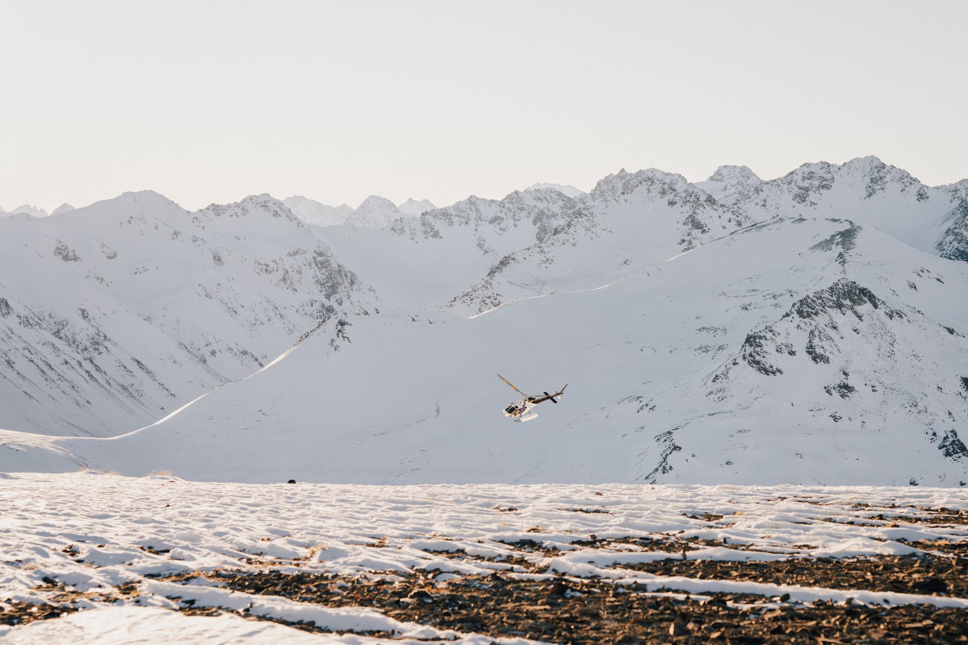 A person is flying over a snowy field with mountains in the background.