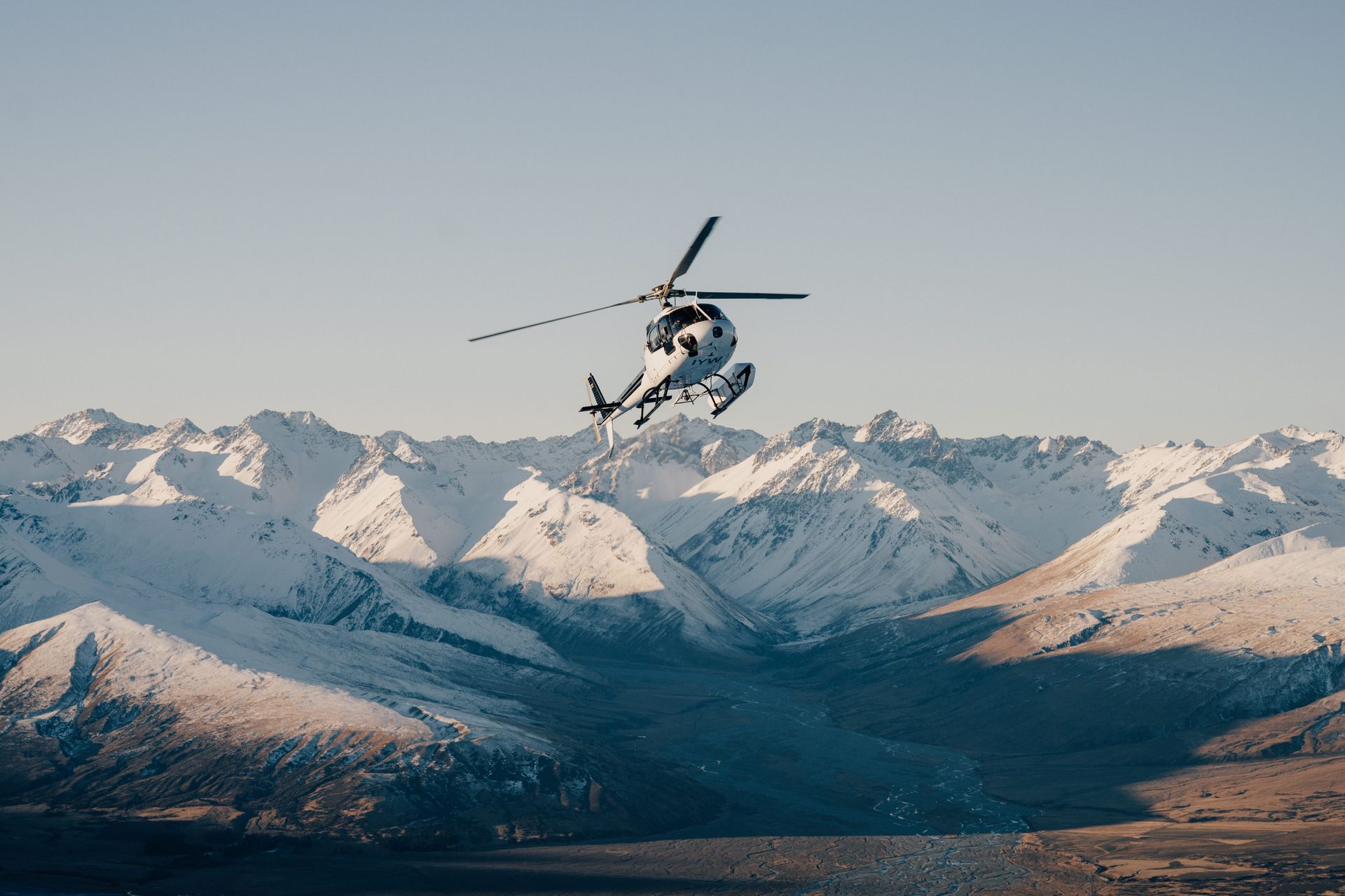 A helicopter is flying over a snowy mountain range.