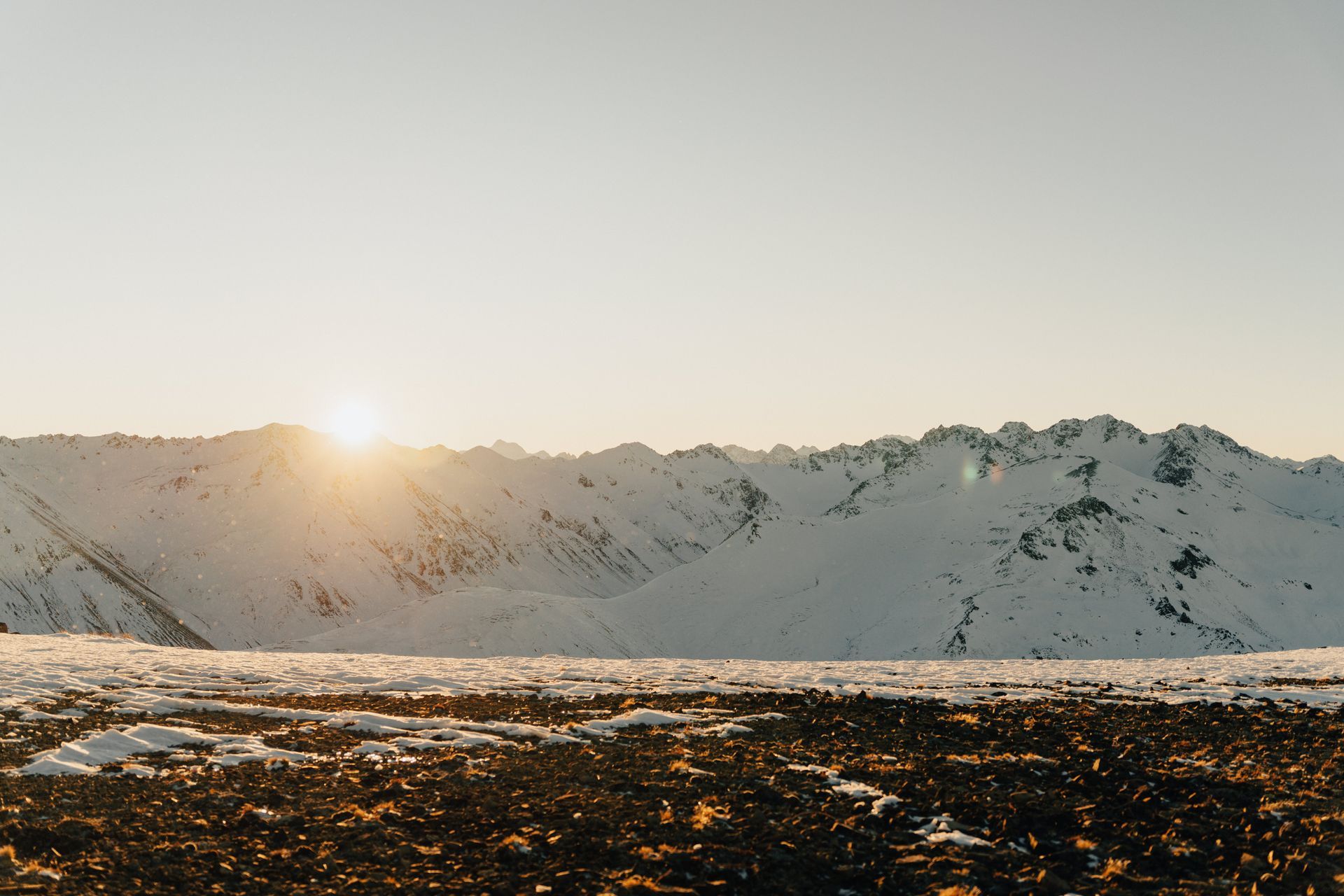 The sun is setting over a snowy mountain range.