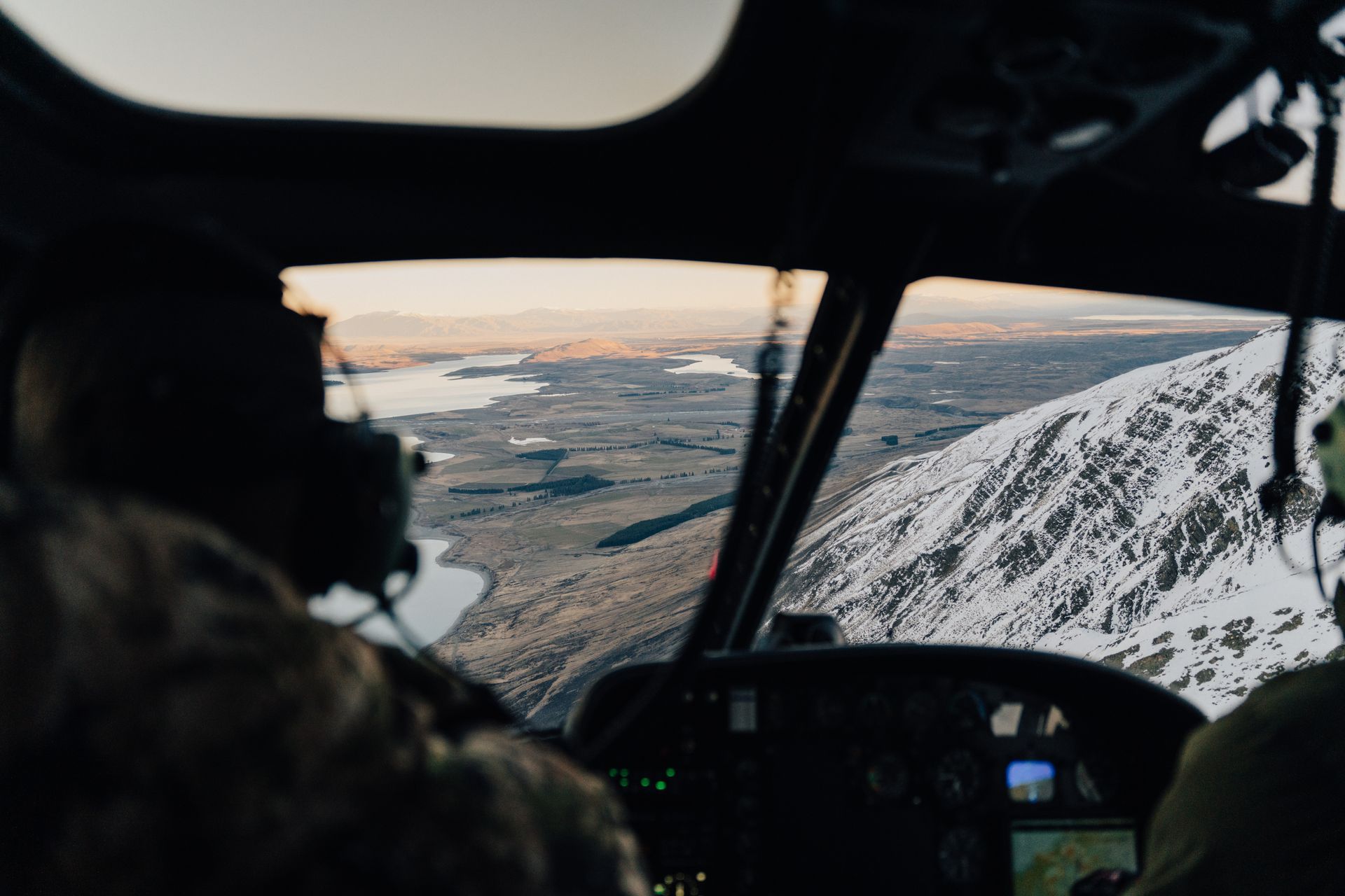 A man is flying a helicopter over a snowy mountain range. High Country Outfitters