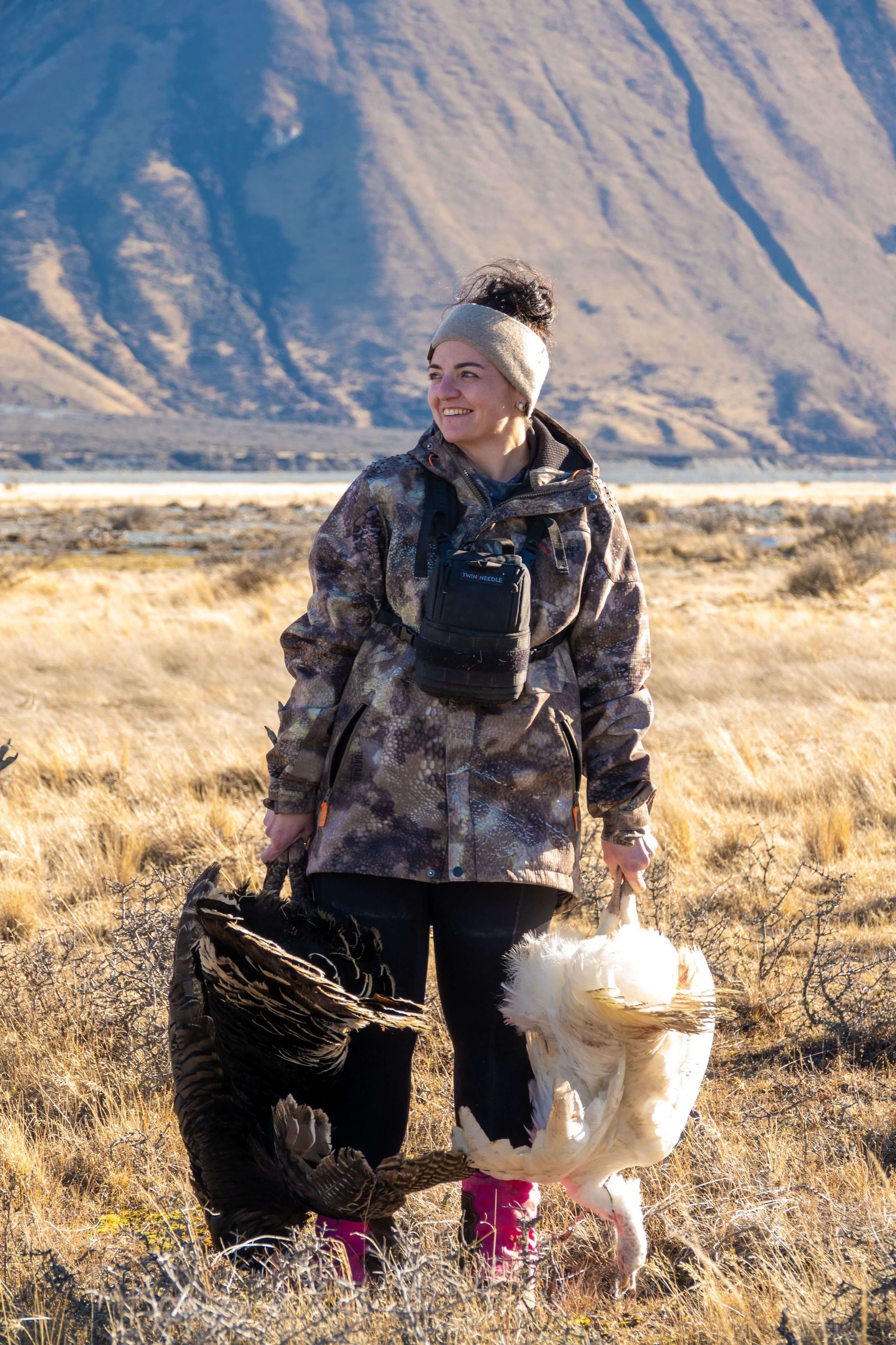 A woman is walking a dog in a field with mountains in the background.High Country Outfitters