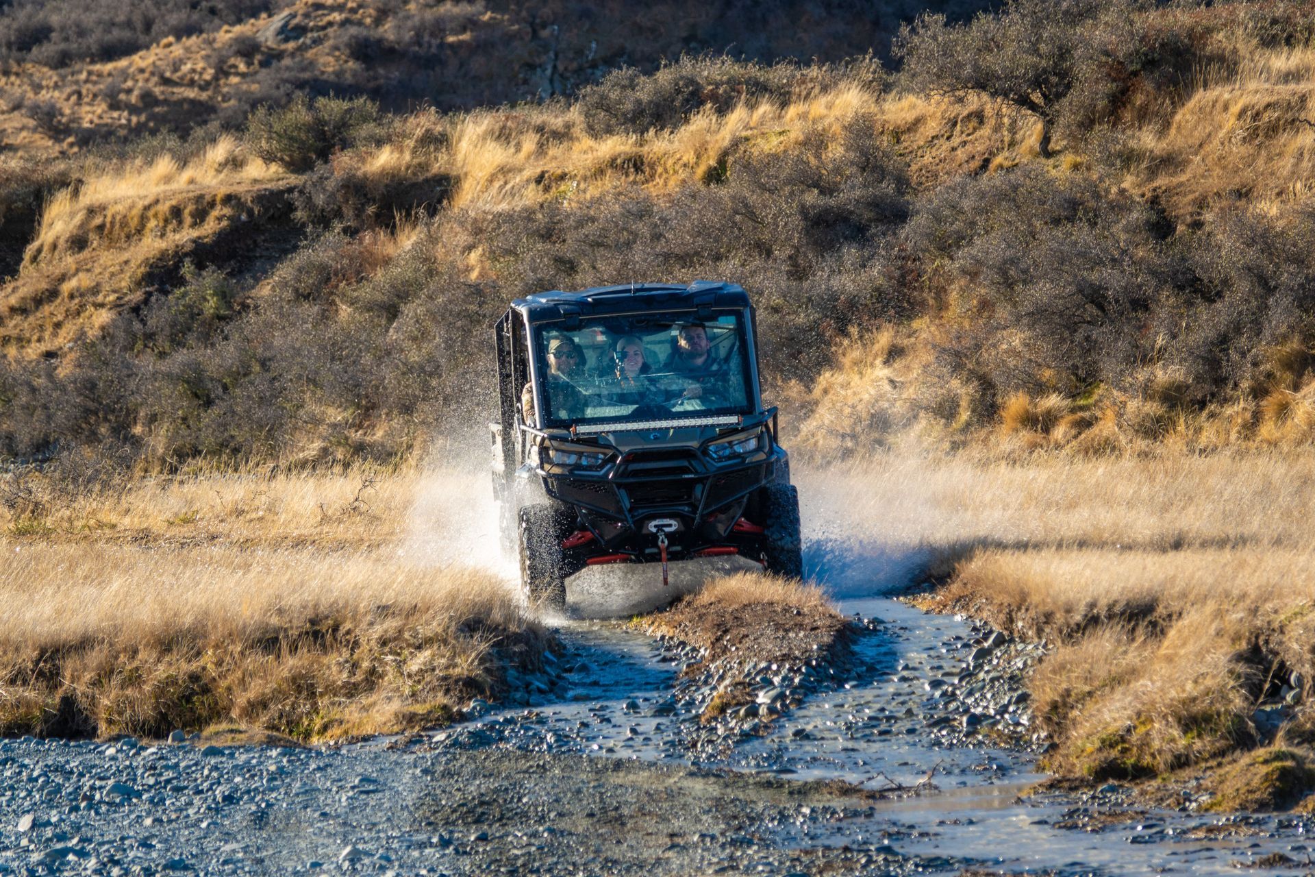 A black atv is driving down a dirt road next to a river. High Country Outfitters